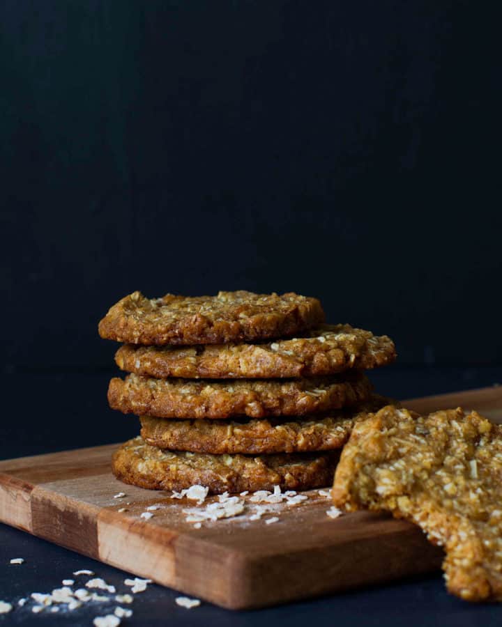 A stack of chewy Anzac biscuits on a wooden board.