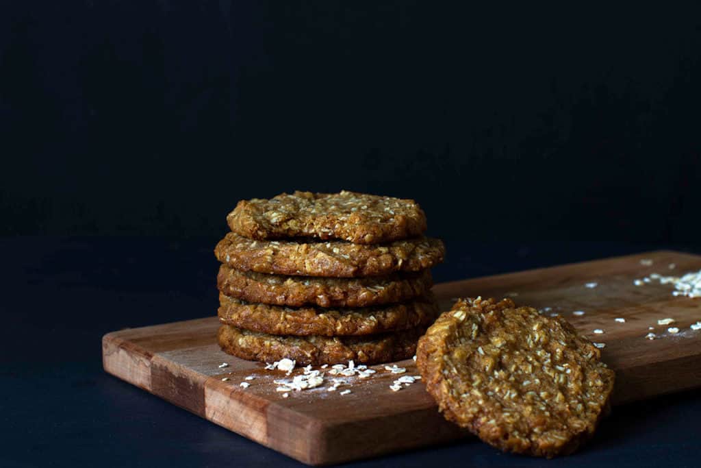 A stack of Chewy Anzac Biscuits on a wooden board