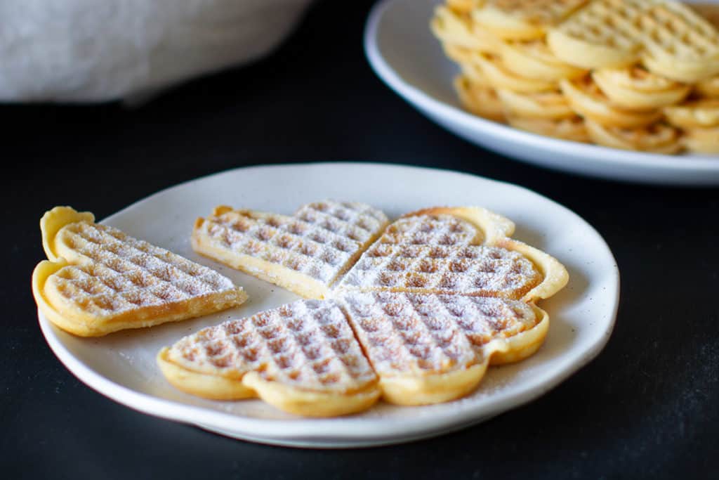Heart-shaped German waffles dusted with icing sugar on a white plate.