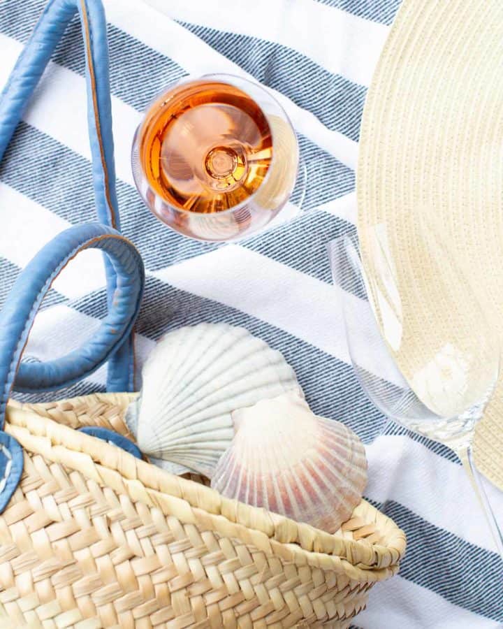 A glass of Rosé with beach gear including a towel, market bag and sea shells