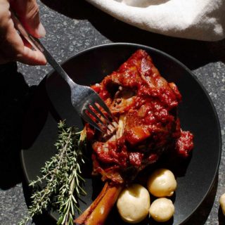 Moroccan Lamb Shanks with potatoes and fresh herbs on a black plate