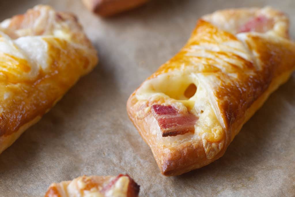 Two zoomed in cheese and bacon turnovers on baking paper