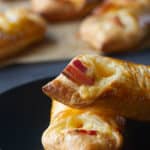 Two zoomed in cheese and bacon turnovers on a black plate