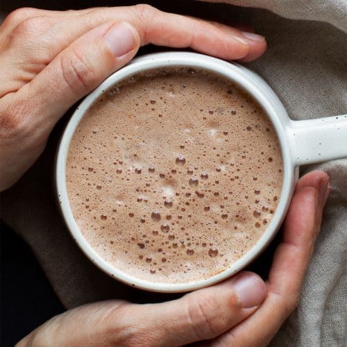 Hot chocolate in a white cup held by two hands.