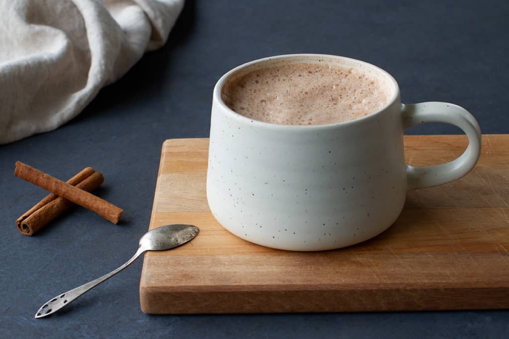 Hot chocolate drink in a cream cup on a wooden board.