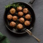 Greek lamb meatballs alongside a sprig of rosemary in a cast iron pan. A green tea towel is to the side.
