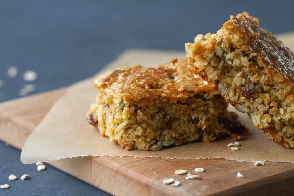 Two nut-free muesli bars on baking paper and a wooden board. 