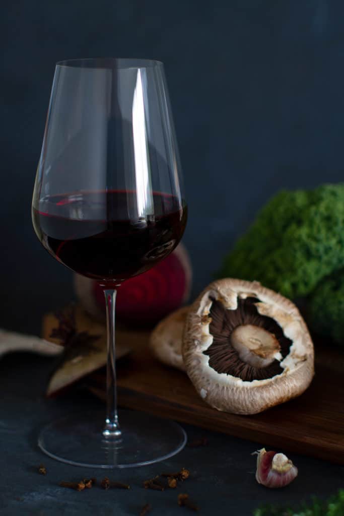 A glass of Pinot Noir in front of a wooden board with fall flavors including a button mushroom, garlic, cloves, beetroot and kale.