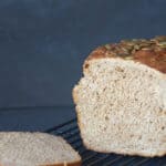 A loaf and slice of soft whey bread on a black cooling rack. Dark background.