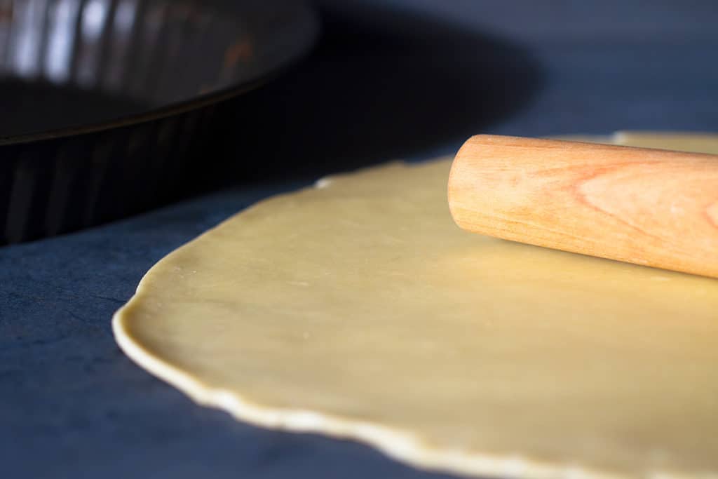 A 3 ingredient pie crust in a pie tin with a rolling pin on a dark background.