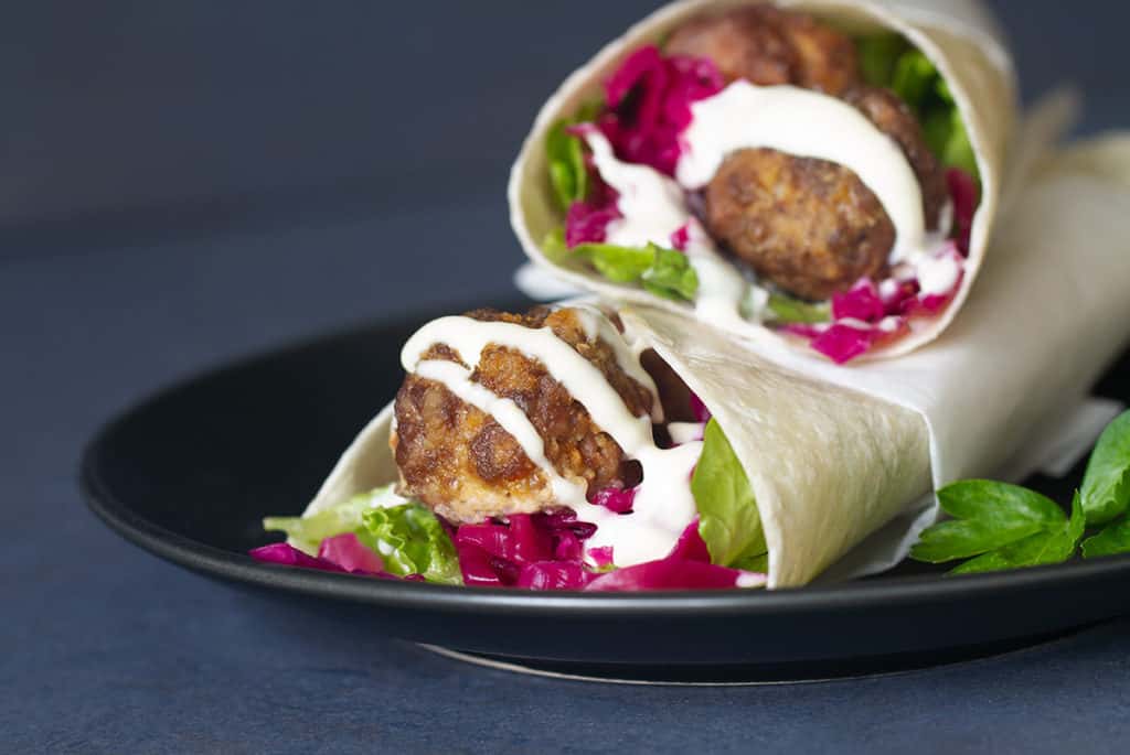 Two meatball wraps on a black plate.