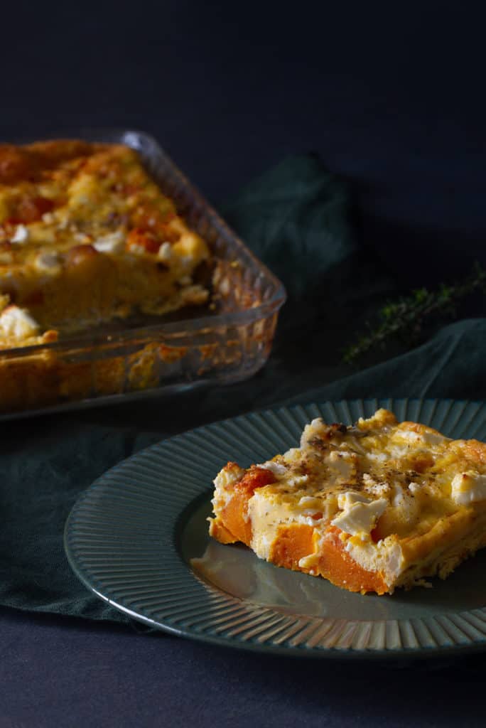 A slice of roasted pumpkin and feta quiche on a green plate. The quiche is blurred out in the back.