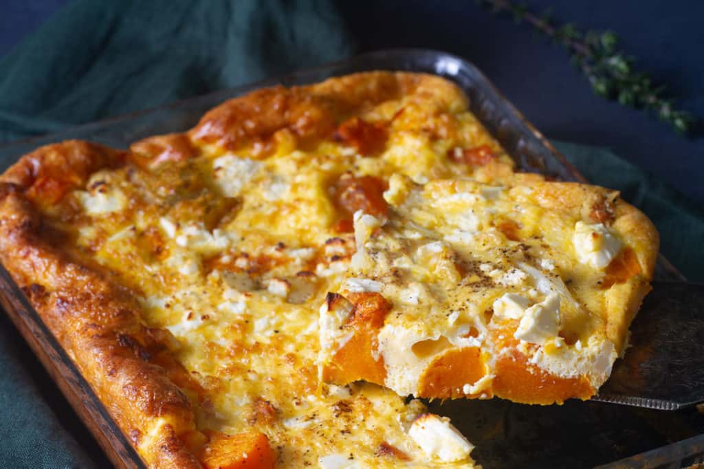 A piece is taken out of a roasted pumpkin and feta quiche.