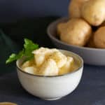 A small bowl of stewed potatoes with parsley. A bowl of potatoes is in the background.