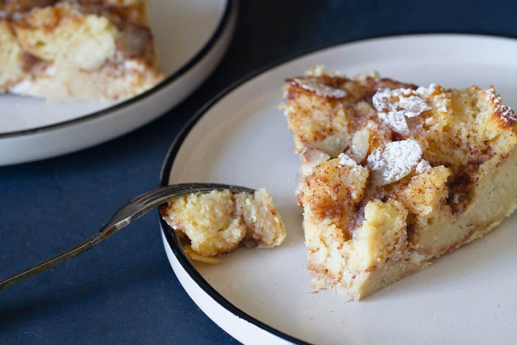 A slice of sourdough bread pudding on a white plate. Another plate is blurred out in the background.