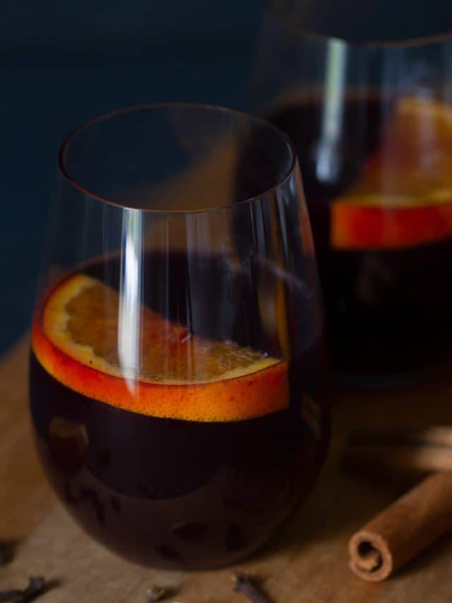 Two glasses of non-alcoholic mulled wine with orange slices in it. Moody scene.