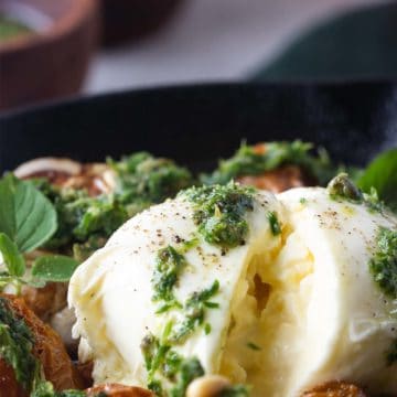 Close-up of a ball of burrata covered with salsa verde and next to slow-roasted tomatoes.