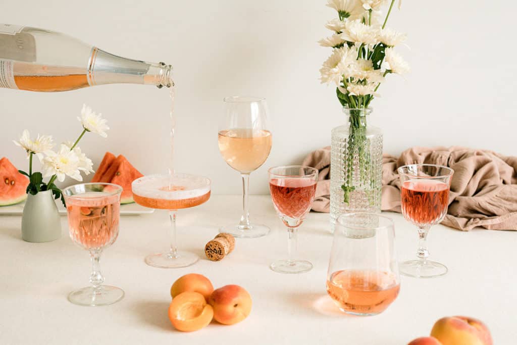 A selection of Rosé wine glasses with some fruit and flowers.