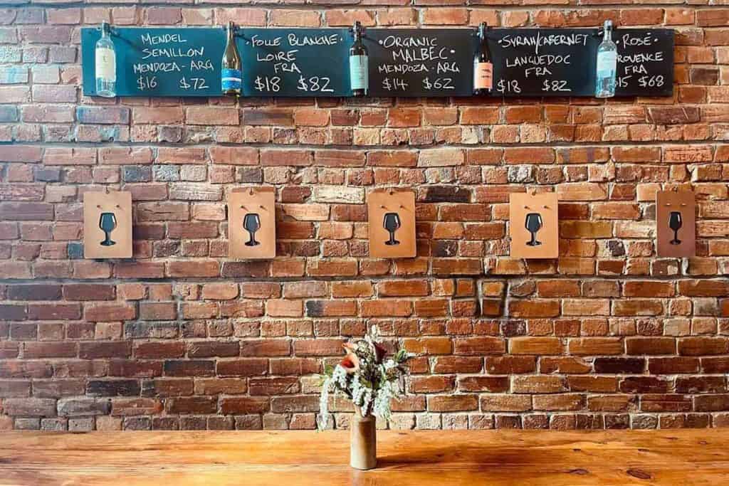 Wooden table at Apéro wine bar in Auckland with a brick wall and wine bottles on the wall.