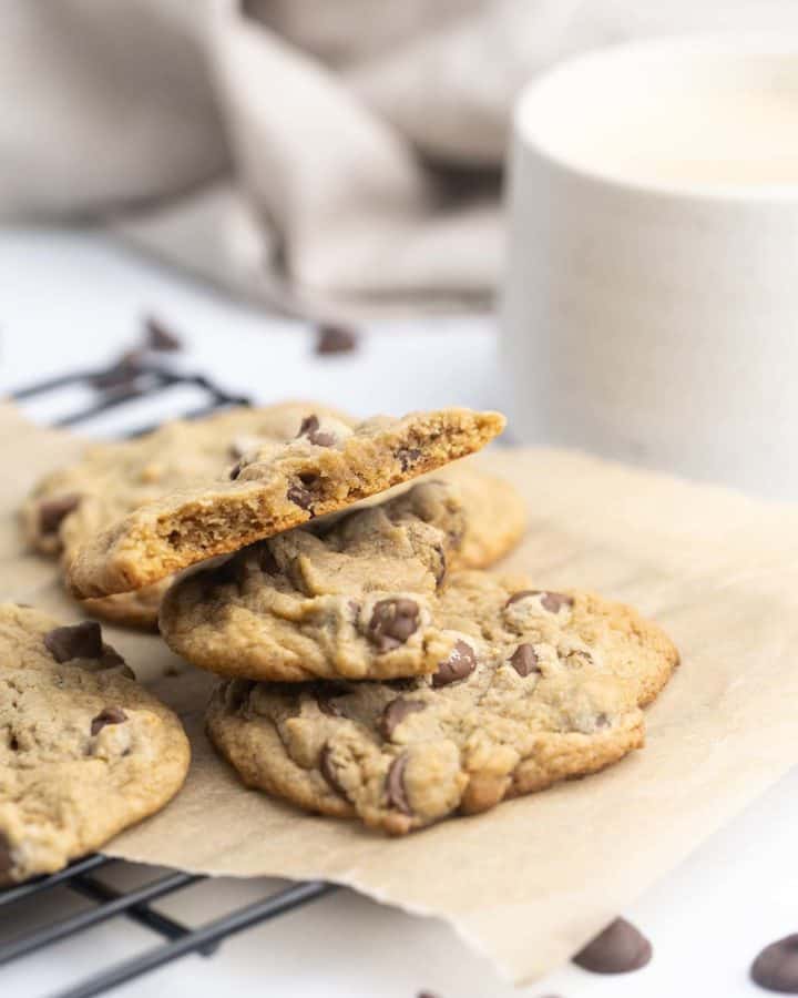 A stack of barley chocolate chip cookies on a cookie tray next to a cup of tea and tea towel.