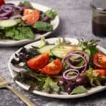 Mixed salads on small white side plates next to glass jar with vinaigrette.