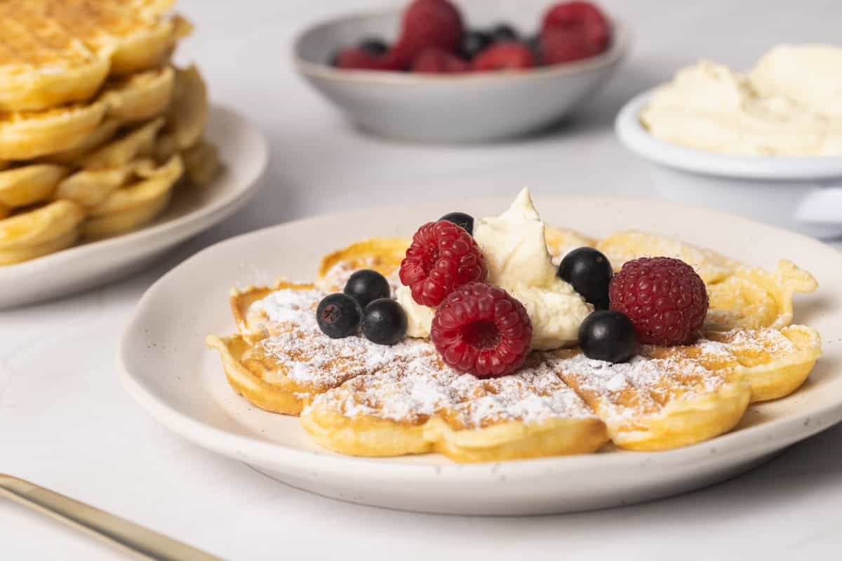 A waffles in a white plate with whipped cream and fresh berries.