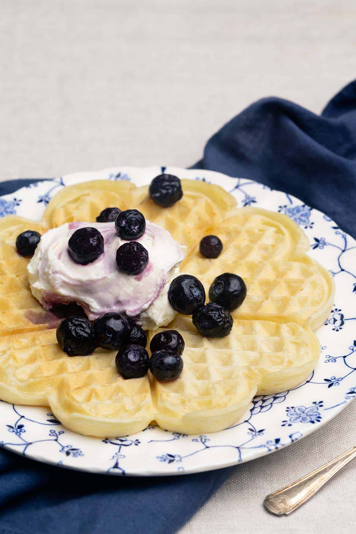 A whey waffle on a patterned plate with Greek yogurt and blueberries.