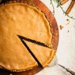 A slice being taken out of a cinnamon pie with pretzel crust. Fall-colored, cozy scene.