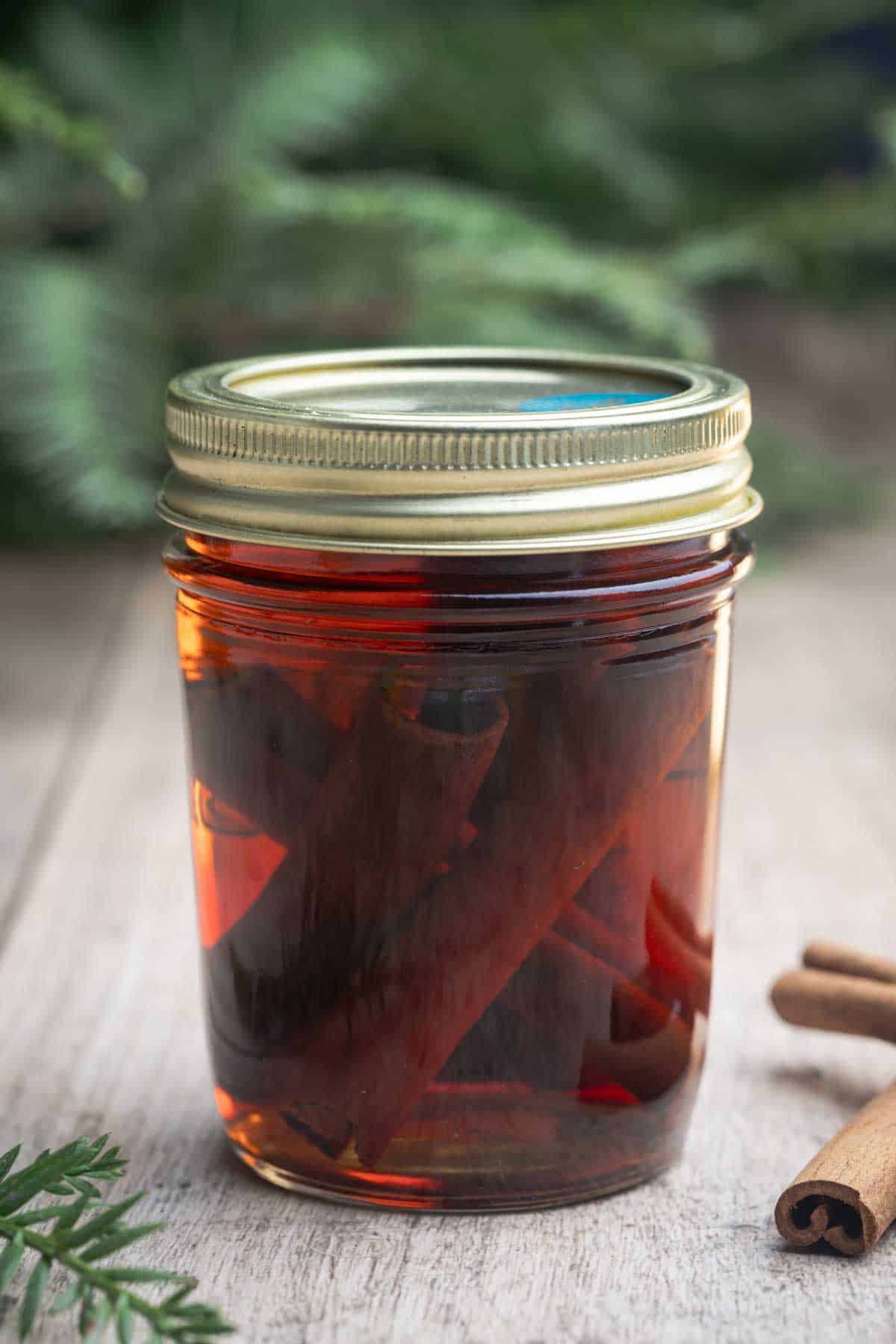 A glass of cinnamon quill extract next to cinnamon quills.