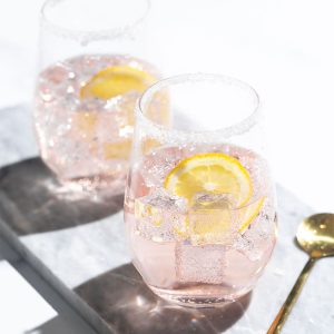 Two Rosé lemonade cocktails on a marble tray next to a golden spoon.