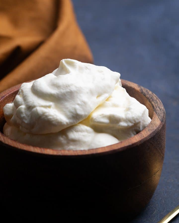 A wooden bowl filled with German whipped cream next to a golden spoon and napkin.