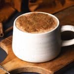A mug of pumpkin spiced hot chocolate on a wooden board.