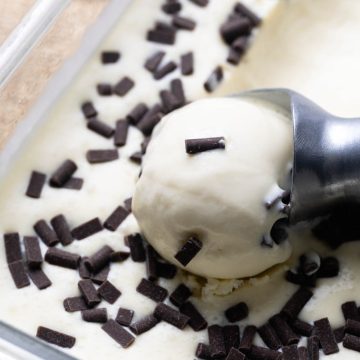 Stracciatella ice cream in a glass container. A portion is being scooped.