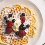 A waffles in a white plate with whipped cream and fresh berries.
