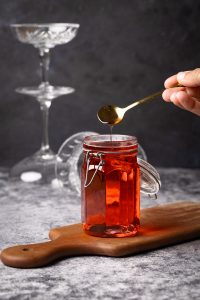 A jar of homemade Rosé simple syrup on a wooden board next to wine glasses.