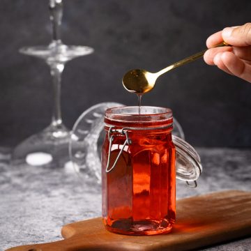 A jar of homemade Rosé simple syrup on a wooden board next to wine glasses.