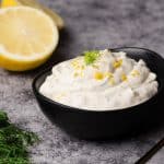 Lemon dill dressing in a black bowl next to lemons and dill.