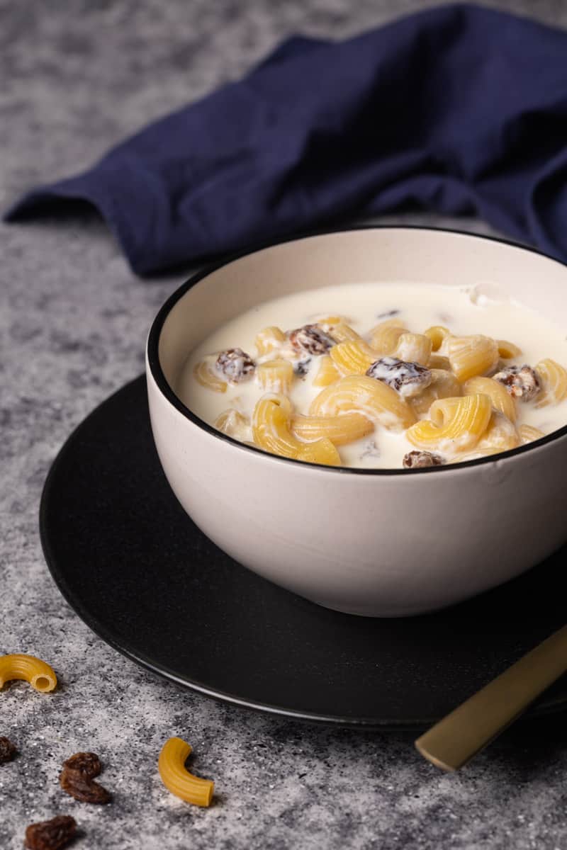A bowl of milk soup with pasta on a black plate.