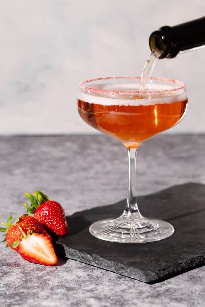 A Rosé margarita cocktail on a shingle slate next to strawberries.