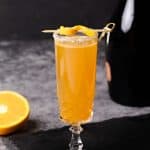 A glass of Rosé mimosa on a slate next to an orange and a bottle of Rosé champagne.