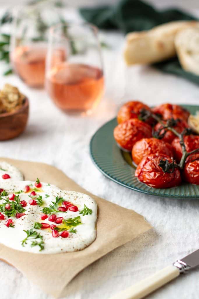 A whipped feta board next to Rosé wine glasses and tomatoes.