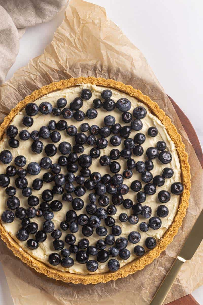 Lemon and blueberry torte on a wooden board next to a linen tea towel.