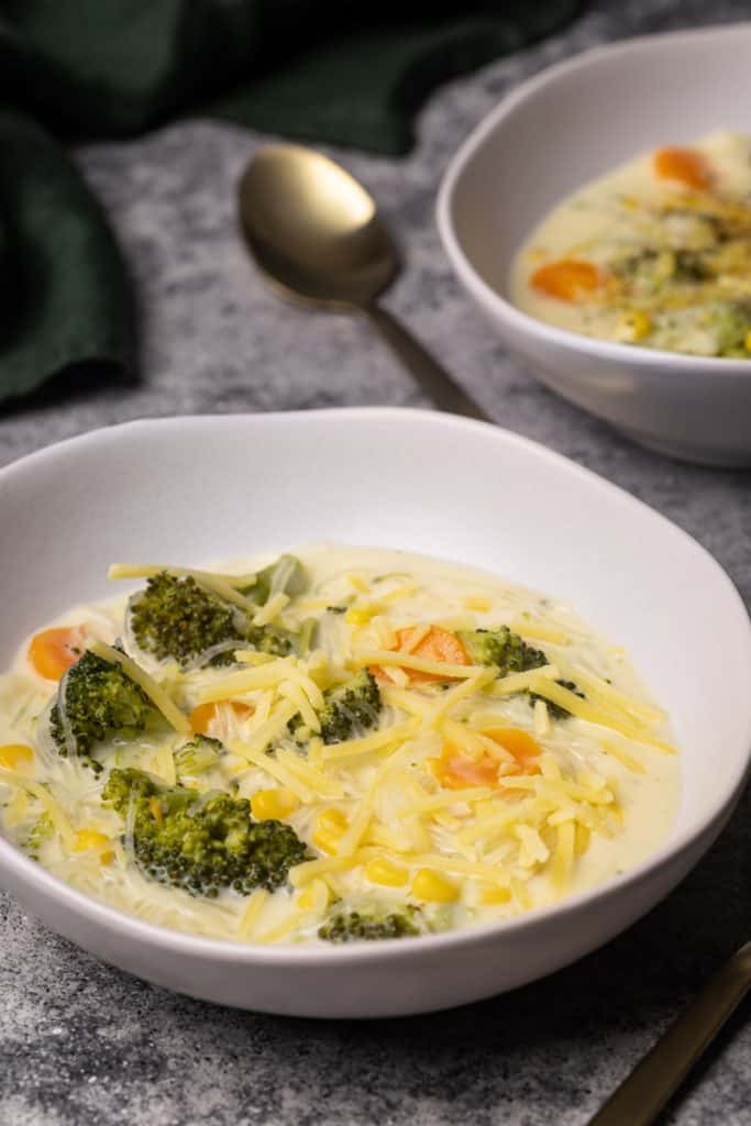 Two bowls filled with broccoli cheese soup with noodles.