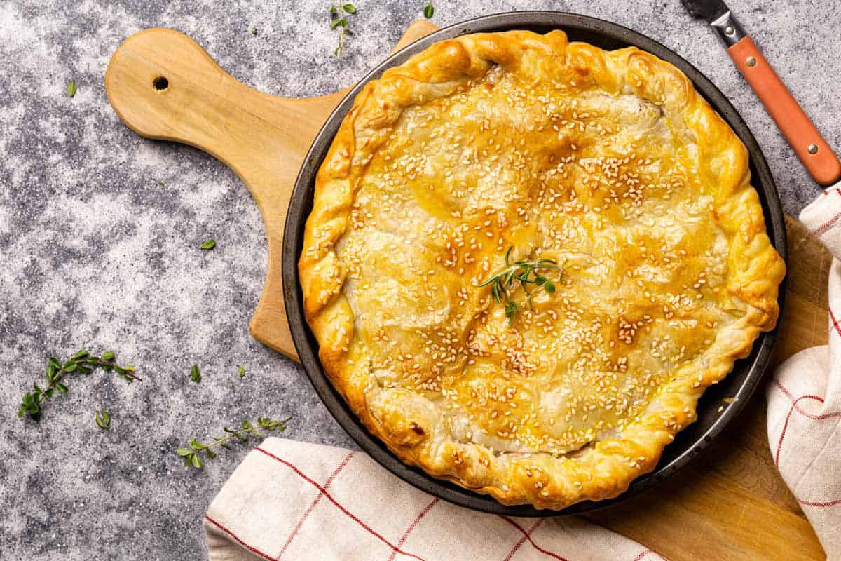 Lamb pie on a wooden board next to a tea towel.