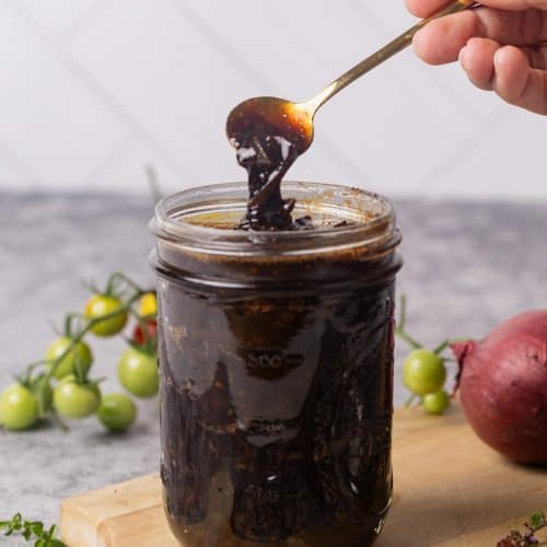 A glass jar filled with caramelized onion tomato jam on a wooden board.