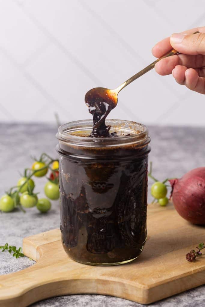 A glass jar filled with caramelized onion tomato jam on a wooden board.
