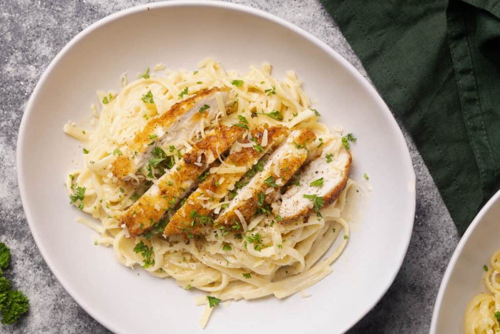 Breaded chicken on creamy linguine pasta in a white bowl next to green napkin.