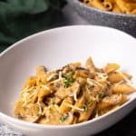 French onion pasta in a white bowl, next to a large pan and green napkin.
