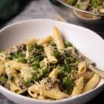 A white bowl filled with ground beef Alfredo pasta next to a large pan.