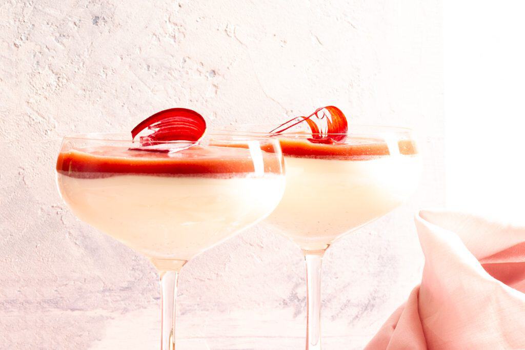 Two champagne coupes filled with vanilla panna cotta and rhubarb coulis.